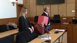 Der Verurteilte im Gerichtsaal verdeckt sein Gesicht mit roter Kladde