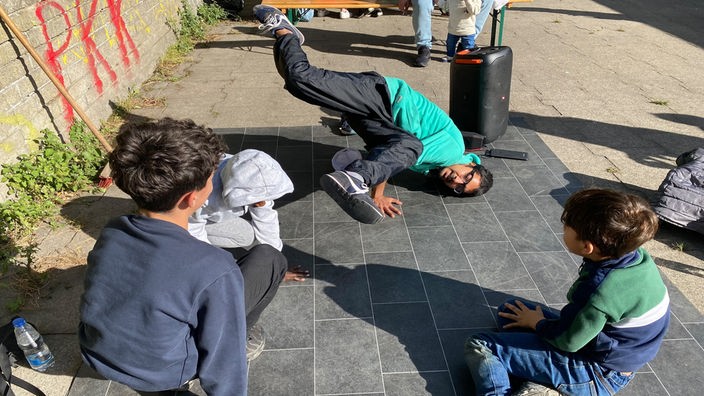 Hip-Hop Künstler Amandip Singh macht Kindern auf dem Boden Tanzfiguren vor