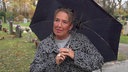 Eine Frau mit einem Regenschirm, in Hintergrund sind Grabsteine zu sehen