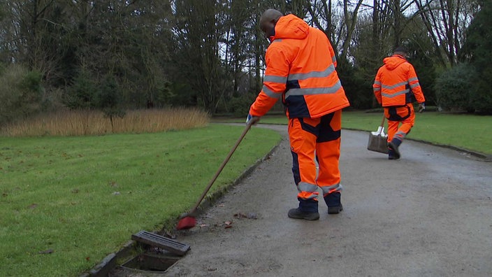 Zwei Personen in Warnkleidung säubern den Weg im Park