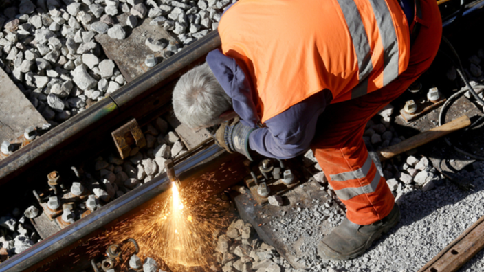 Ein Bauarbeiter schweißt ein Stück Schiene auf einer Bahn-Baustelle