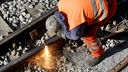 Ein Bauarbeiter schweißt ein Stück Schiene auf einer Bahn-Baustelle