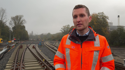 Ein Mann steht mit einer orangenen Jacke an einer Bahnstrecke