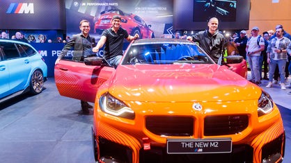 Drei Männer präsentieren einen orangefarbenen, getunten BMW M2