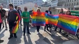 Menschen stehen mit Regenbogenflaggen bei der Verlegung der Stolperschwelle für verfolgte Homosexuelle in der NS-Zeit in Bochum
