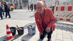 Jürgen Wenke, Psychologe aus Bochum, kniet neben der frisch verlegten Stolperschwelle, für die er sich eingesetzt hat