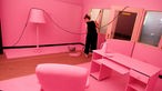 Eine Frau bestreicht den Fußboden eines Zimmers in Rosa. Alles andere in dem Zimmer ist bereits rosa.