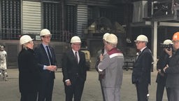 Bundespräsident Steinmeier steht in einer Gruppe von Personen und unterhält sich. Alle tragen einen weißen Helm.