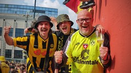 Drei Fans in schwarz-gelben Shirts und Trikots auf dem Dortmunder Hansaplatz