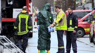 Auf dem Foto sind zwei Männer mit grünen Schutzanzügen und Atemschutzmasken. Daneben stehen gewöhnlich ausgestattete Männer der Feuerwehr Dortmund.