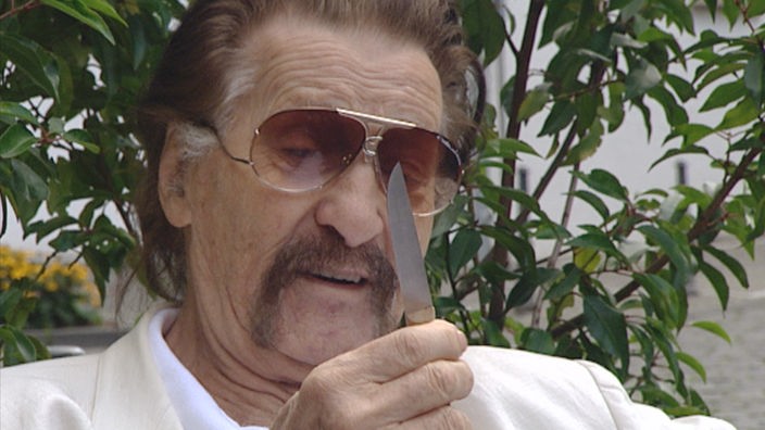 Ein Mann mit Sonnenbrille begutachtet ein Messer