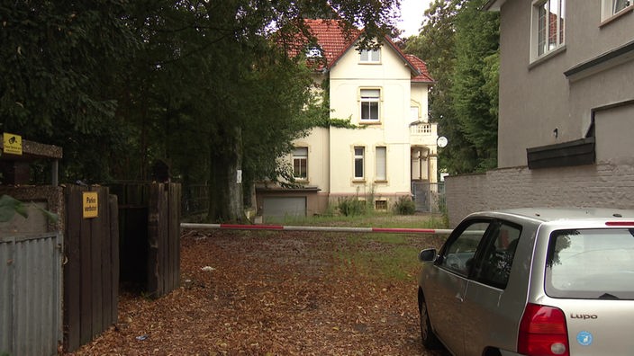 Blick auf Wohnhaus mit heller Fassade in einem Hinterhof, davor eine Schranke und ein silbernes Auto