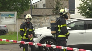 Auf dem Foto sind zwei Feuerwehrmänner, die mit Atemschutzmasken hinter einem Absperrband herlaufen.