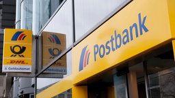 Auf dem Foto ist ein Eingang, über dem "Postbank" in blauer Schrift auf gelbem Grund steht.