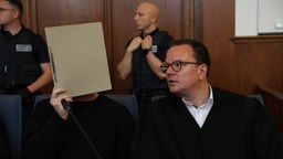 Im Gerichtssaal verbirgt der angeklagte Schütze sein Gesicht hinter einer Mappe, neben ihm sitzt sein Verteidiger Christoph Krekeler