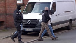SEK-Beamte führen einen festgenommenen Mann ab, im Hintergrund steht ein weißer Lieferwagen