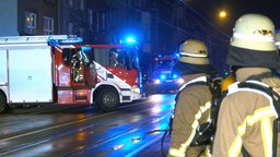 Zwei Feuerwehrmänner mit zwei Einsatzfahrzeugen auf einer Straße bei Nacht