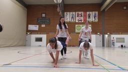 Vier Schülerinnen trainieren die Sportübung "Schubkarre"
