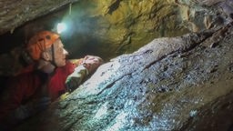 Ein Forscher mit Stirmlampe steht in der neu entdeckten Höhle in Ennepetal