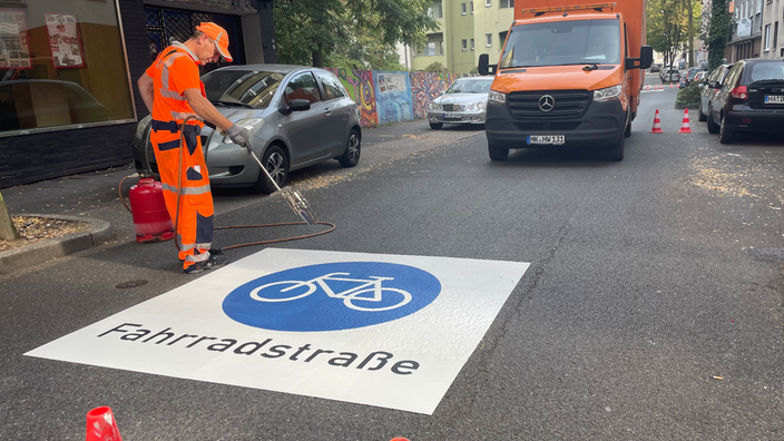 Ein Mann im orangen Anzug bringt ein Schild mit der Aufschrift Fahrradstraße auf der Fahrbahn auf