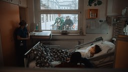 Medin liegt in seinem Bett, neben ihm kniet Superman, ein Ninja-Turtle steht vor dem Fenster in einer Drehleiter.