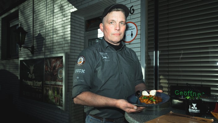 Jürgen Bickert steht vor seiner Fleischerei in der Hand hält er einen Teller mit Nutria-Ragout