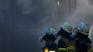 Drei Feuerwehrleute stehen mit Gasmasken vor einer dicken Rauchwolke.