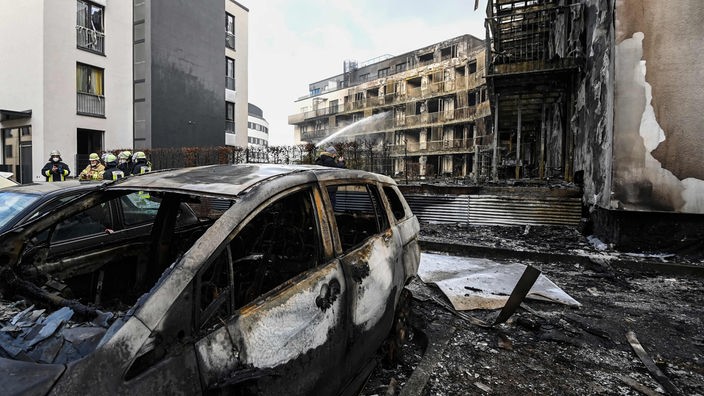 Der ausgebrannte Wohnkomplex im hellen und ein ausgebranntes Auto