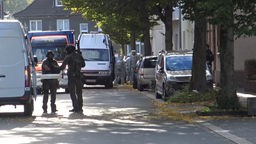 Einsatzwagen und Einsatzkräfte in Schutzausrüstung stehen auf einer Straße in einem Wohngebiet