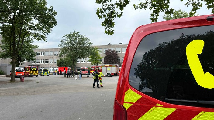 Mehrere Feuerwehrautos, Rettungswagen und ein Polizeiauto stehen vor einem Schulgebäude