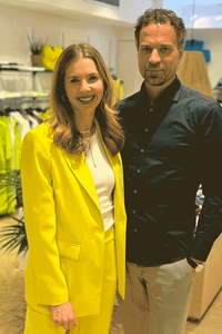 Auf dem Foto sind Maya Schleuter und ihr Ehemann Christian in ihrem Laden zu sehen. Im Hintergrund hängen GArderobenstangen mit Frauenleidung.