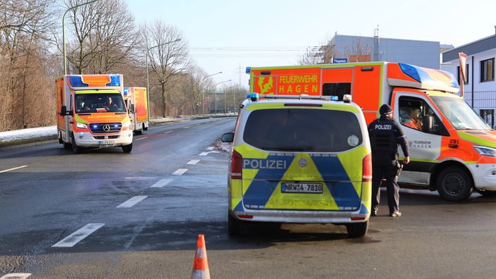 Auf dem Foto ist eine Straße, auf der ein Polizei-Bulli und ein Feuerwehr-Wagen stehen. Daneben fahren Feuerwehrautos ein.