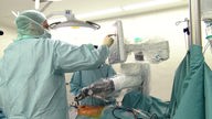 Menschen in Operationskleidung vor dem OP-Tisch, dazwischen ein maschineller Arm
