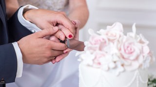 Zwei Hände eines Brautpaares, die eine Hochzeitstorte anschneiden