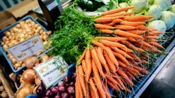 Karotten und Zwiebeln liegen an einem Obststand auf einem Wochenmarkt