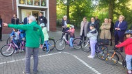 Grundschüler mit stehen mit Fahrrad und Helm auf einem aufgemalten Parcours, drumherum Erwachsene