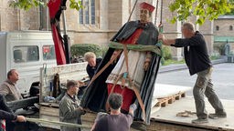 Mehrere Männer laden die Statue von Kardinal Hengsbach vor dem Essener Dom auf einen Anhänger.