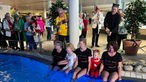 Drei Frauen und zwei Kinder sitzen angezogen am Rand eines Schwimmbeckens