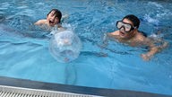 Zwei Kinder im Wasser schwimmen auf Ball zu