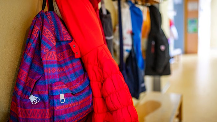 An einer Garderobe in einem Kindergarten hängen Jacken und Rucksäcke von Kindern