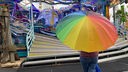 Eine Frau steht mit einem regenbogenfarbenen Schirm vor einem Karussel auf der Cranger Kirmes
