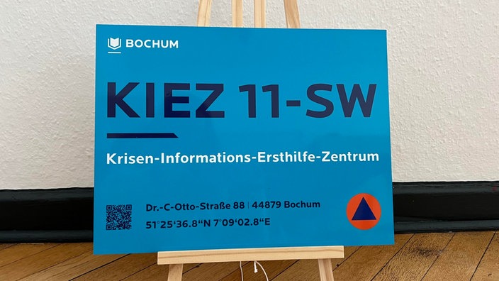 Das Bild zeigt ein blaues Schild der Stadt Bochum, auf dem "Hinweisschild zum Krisen-Informations-Ersthilfe-Zentrum", sowie die Adresse und die genauen Längen- und Breitengrade des Zentrums stehen.