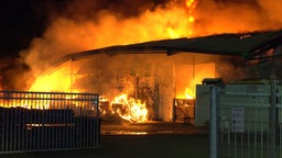 Die Lagerhalle in Hünxe in Brand, man sieht Flammen und Rauch, es ist dunkel