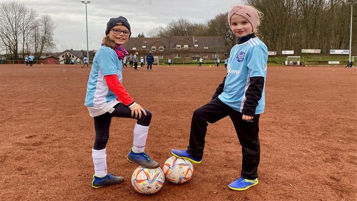 Zwei achtjährige Mädchen stehen mit Ball auf dem Fußballplatz