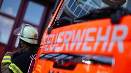 Ein Feuerwehrmann steht neben einem Feuerwehrauto, auf dem in großen weißen Buchstaben "Feuerwehr" geschrieben steht