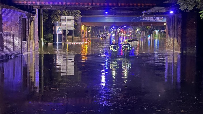 Ausschnitt Straße in Gelsenkirchen-Schalke, Feuerwehrmänner laufen durch das Wasser, das kniehoch steht