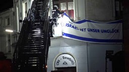 Ein Feuerwehrmann entfernt eine Flagge an einem Dorstfelder Wohnhaus. Auf der Flagge steht "Israel ist unser Unglück"