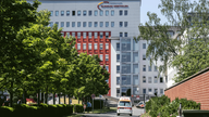 Im Hintergrund ist das Gebäude des Klinikums Westfalen in Dortmund zu sehen. Vorne im Bild sieht man eine straße, auf der ein Krankenwagen Richtung Kamera fährt.
