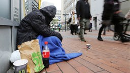 Ein Obdachloser sitzt zusammengesunken mit seinen Habseligkeiten am Rand einer Dortmunder Einkaufsstraße 