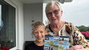 Oma Renate und ihr Enkel Maximilian zeigen die Postkarte in die Kamera